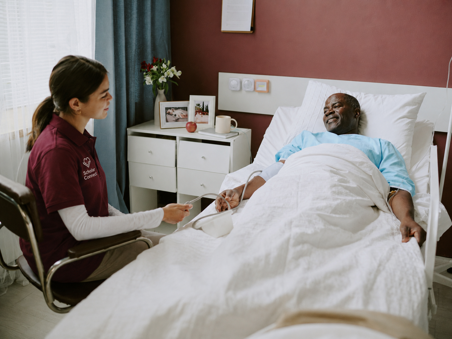 A scholar sits beside a patient, reading together during a quiet shift moment.